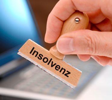 Mensch hält Stempel mit dem Aufdruck Insolvenz in der Hand
