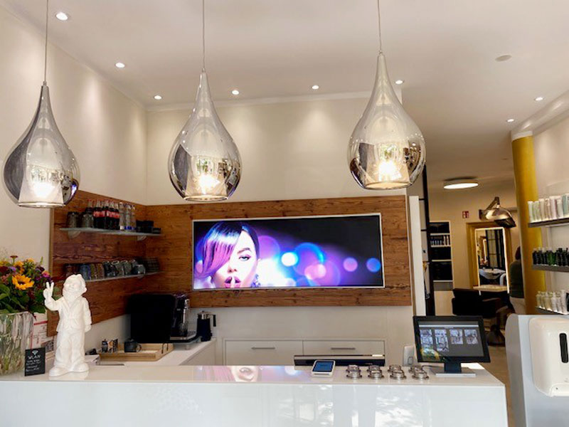 Kassenbereich mit großem Display an der Wand eines Salons.