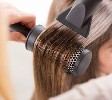 Friseur föhnt Haare der Kundin über Rundbürste