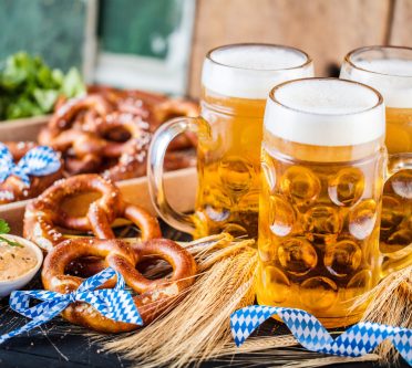 Bierkrüge, Brezeln und Obazda auf einem bayerisch geschmückten Tisch