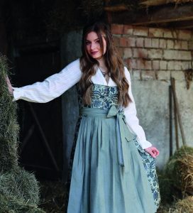 Das Bild zeigt eine Frau im Dirndl, mit langen, gewellten, halb hochgesteckten Haaren.