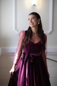 Das Bild zeigt eine Frau im dunkelroten Dirndl, mit halboffenen, langen dunklen Haaren.