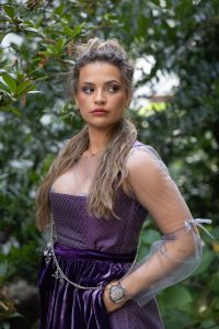 Das Bild zeigt eine Frau in einem lilafarbenen Dirndl mit hochgesteckten Haaren.