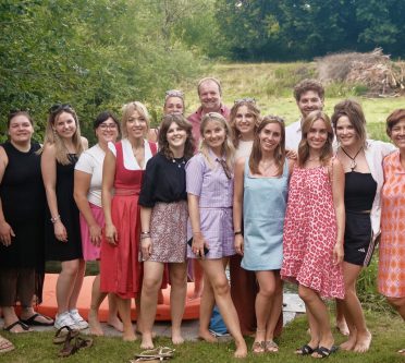 Gruppenbild mit 17 Menschen auf einer Wiese. Im Hintergrund sind Büsche und Bäume zu sehen.