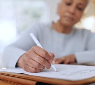 AdobeStock_671437614 Frau sitzt am Tisch und unterzeichnet ein Dokument
