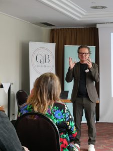 Heiko Schneider steht vor Publikum, Im Hintergrund ein Club der Besten Banner