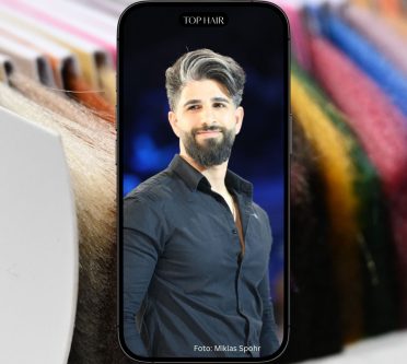 Foto von einem jungen Mann mit grauen Haaren, das auf einem Smartphone zu sehen ist. Im Hintergrund des Handys sieht man einen Farbfächer zur Beratung beim Friseur.