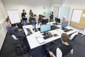 Jurymitglieder sitzen von PCs und hören TOP HAIR-Chefredakteurin Rebecca Kandler beim Briefing zu
