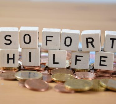 Holzwürfel bilden das Wort Soforthilfe und stehen auf Geldmünzen- und scheinen