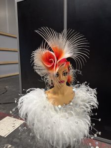 Kunstvoll hochgesteckte Haare in Organge, Silber mit Lila-Strähnen am geschminkten Übungskopf