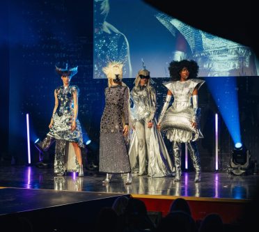 Vier Frauen in avantgardistisch silber glitzendem Outfit zeigen voluminöse Frisuren auf der Bühne für eine Redken Show.