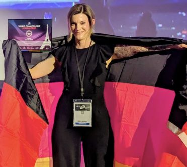 Eine junge blonde und lächelnde Frau in Schwarz gekleidet, zeigt sich mit der deutschen Flagge