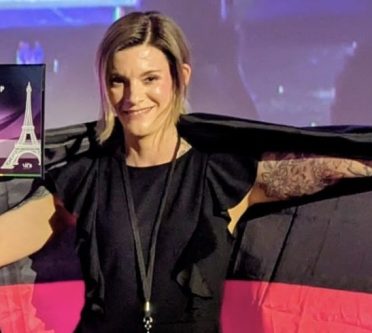 Eine junge blonde und lächelnde Frau in Schwarz gekleidet, zeigt sich mit der deutschen Flagge