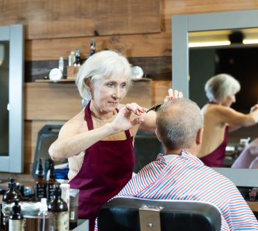 Ältere Friseurin schneidet einem Kunden im Barbershop die Haare