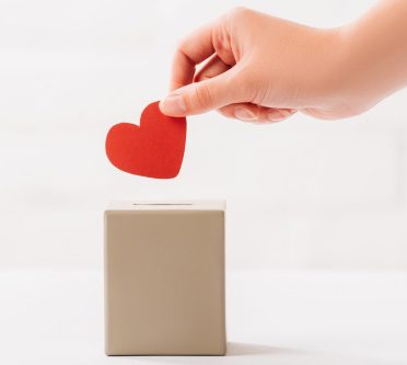 Hand wirft rotes Hertz in Spardose