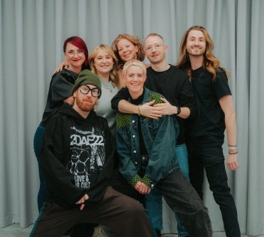 Teilnehmer*innen stehen in Gruppe zusammen und lächeln in die Kamera