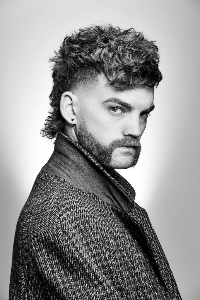 Das Foto zeigt einen Mann mit Mullet Frisur und Mutton Chops Beard