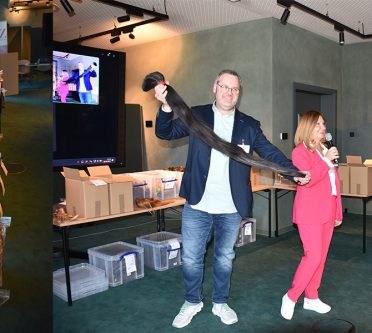 Zöpfe in Kartons, Mann hält abgeschnittenen Zopf, Frau mit Mikrofon