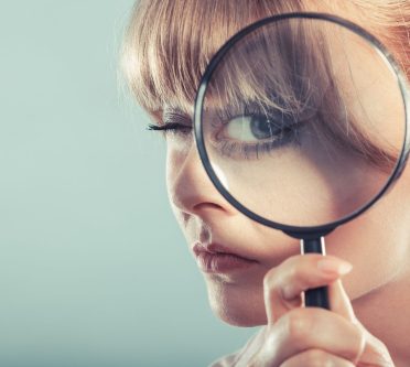 Frau hält Lupe vor ein Auge