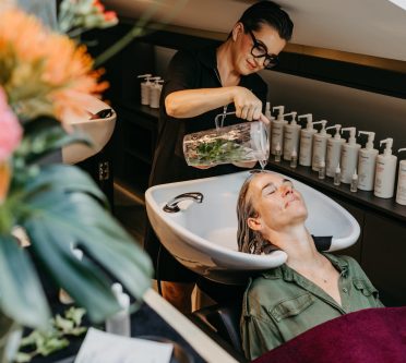 Frau macht Stirnguss mit Karaffe am Waschplatz im Friseursalon