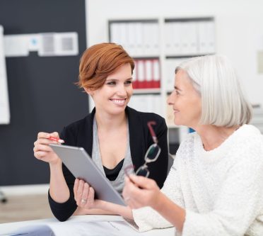 Ältere Frau und jüngere Frau besprechen sich in einem Büro. Unterlagen auf dem Tisch