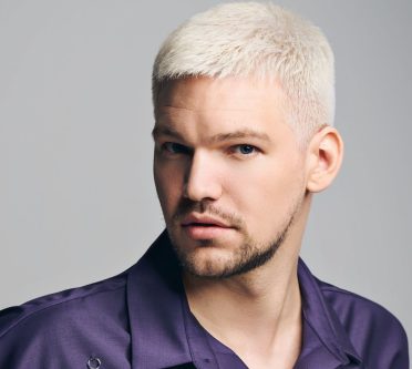 Das Foto zeigt den Kopf eines Mannes mit blondierten, kurzen Haaren und einem Bart