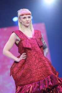 Workshop-Trend Stufen 10 Frau mit stark gestuftem Haar und markantem Pony im rotem Outfit auf einem Laufsteg