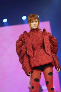 Workshop-Trend Stufen 2 Frau mit kupferrotem, kurzem Haar und rotem Outfit auf einem Laufsteg