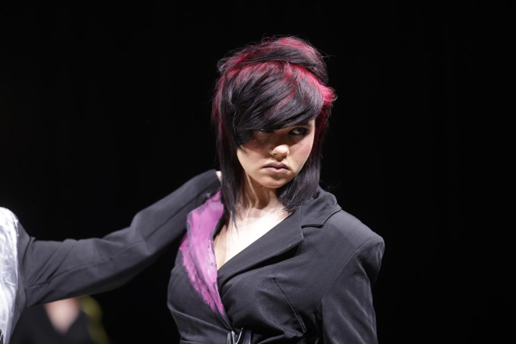 Eine Frau mit Statement-Haarfarbe in Magenta und Schwarz auf einer Bühne, Colour Root-Effekt