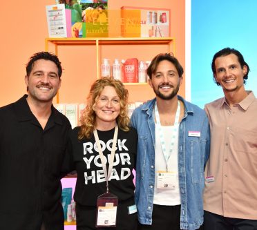 Vier Menschen stehen vor einer Messe-Wand und lächeln in die Kamera