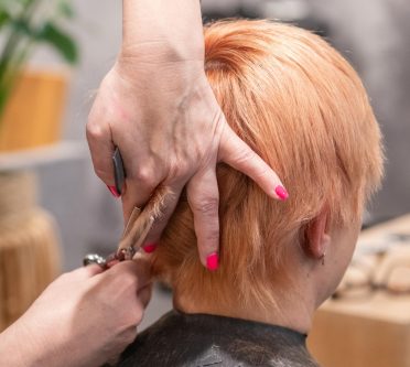 Frau sitzt mit rötlichblondem Haar bekommt Haare geschnitten
