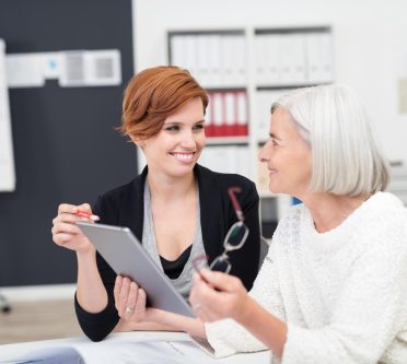 Jüngere und ältere Frau sitzen in einem Büro und besprechen sich am Tablet
