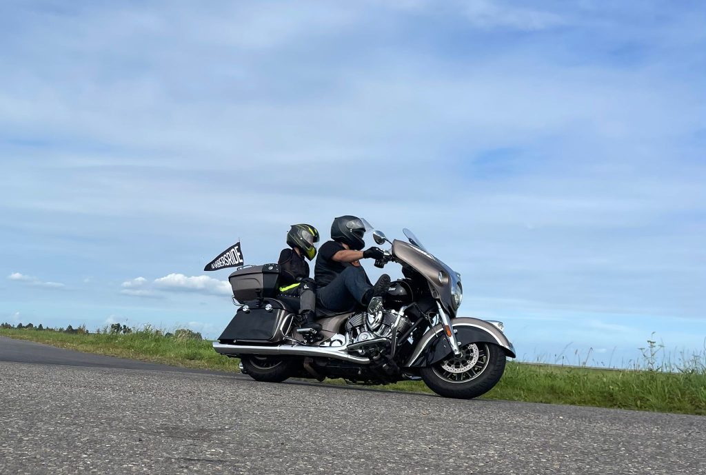 Barbersride rollt 2026 wieder für schwerkranke Kinder 3 Man sieht ein schweres Motarrad, auf dem zwei Personen mit Helm fahren. Am Motorrad ist ein Wimpel mit der Aufschrift Barbersride befestigt.