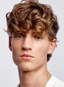 Trend-Kollektion Label.M 6 Ein Mann mit lockig ins Gesicht gestyltem, längeren Haarschnitt in dunklerem Blond.