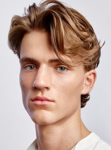 Trend-Kollektion Label.M 5 Ein Mann mit schwungvoll aus dem Gesicht gestyltem, längeren Haarschnitt in dunklerem Blond.