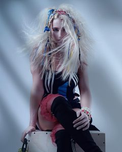 Kollektion_Mood_Tracey_Ann_Smith 1 Ein Model mit langem, blonden, welligem Haar, in das bunte Bänder geflochten sind