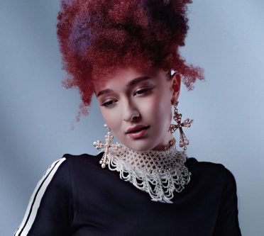 Ein Model mit voluminös hochgestecktem Coily Hair in dunklen Rot- und Violetttönen