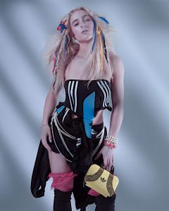 Kollektion_Mood_Tracey_Ann_Smith 7 Ein Model mit langem, blonden, welligem Haar, in das bunte Bänder geflochten sind