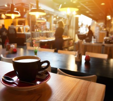 Das Bild zeigt eine Tasse Kaffee auf einem Tisch in einem Café