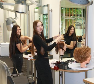zwei junge Frauen an Frisierköpen vor einem Spiegel