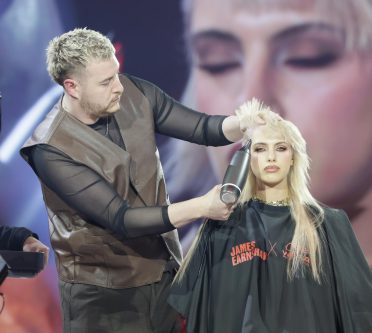 Zu sehen ist James Earnshaw, der vor der Kamera ein blondes Model föhnt.