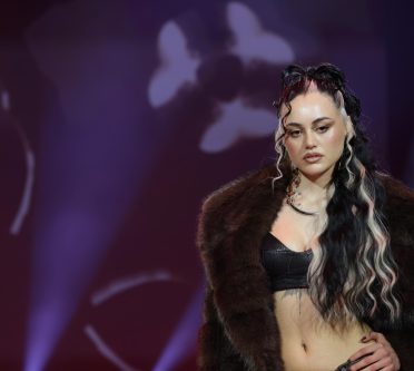 Das Bild zeigt eine Frau mit langen Haaren im Half Bun Style. Die schwarzen Haare sind mit markanten hellblonden Strähnen unterbrochen