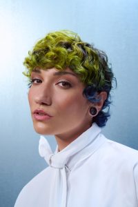 Trend Alcina 7 Kurzer, stark texturierter Lockenlook mit blau-grünen Farbverläufen und längerer, bewegter Deckhaarpartie.