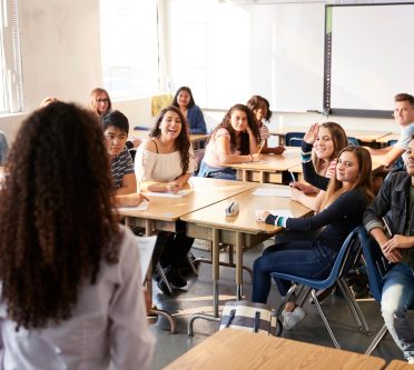 Lehrerin von hinten vor einer Schulklasse mit Jugendlichen