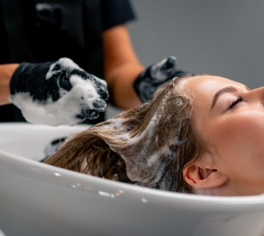 Hand die am Waschbecken einer Frau die Haare wäscht