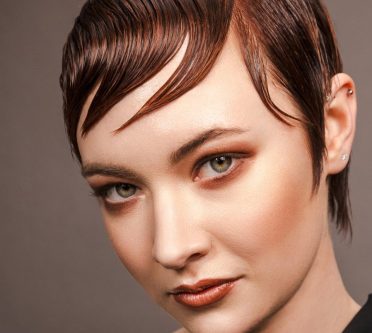 Kurzer, dunkler Pixie Cut, glatt im Wet Look gestylt, mit seitlich über die Stirn gelegtem Pony