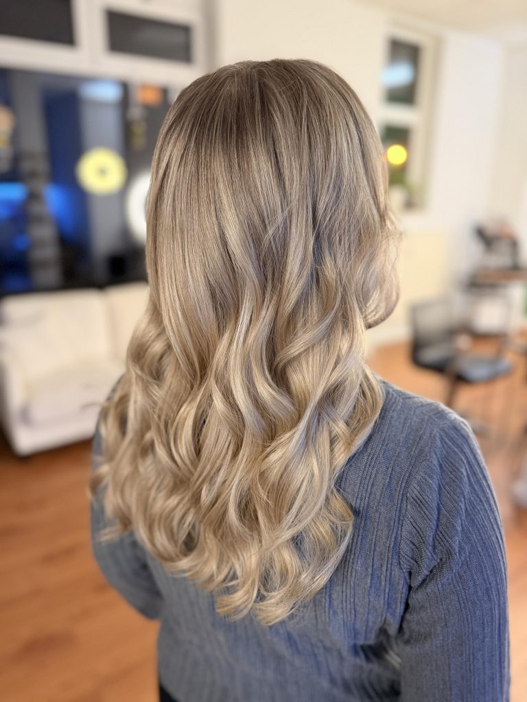 Das Foto zeigt lange, blonde, in Längen und Spitzen gewellte Haare im Farbton Metallic Blond